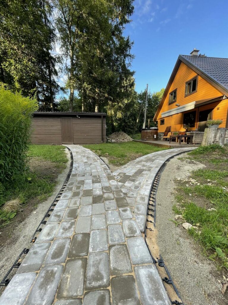 Kaunis kiviteekattega jalgtee kahvliga metsiku looduse taustal kaasaegse puumaja ees - Saku Ehituse täpne ja kvaliteetne kiviteede paigaldus.
