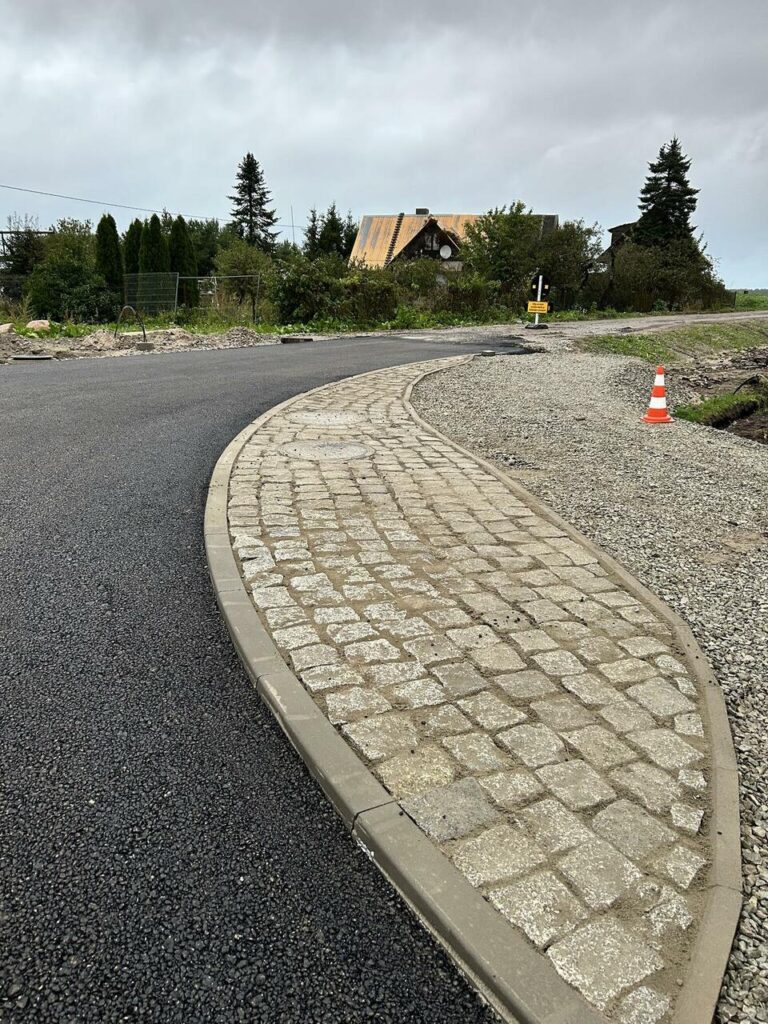 Uus, hoolikalt rajatud asfalt- ja sillutiskivi teeäär maapiirkonnas, rõhutades kvaliteetset teetööde ja sillutusteenuste teostust - Saku Ehitus tee- ja sillutustööd.